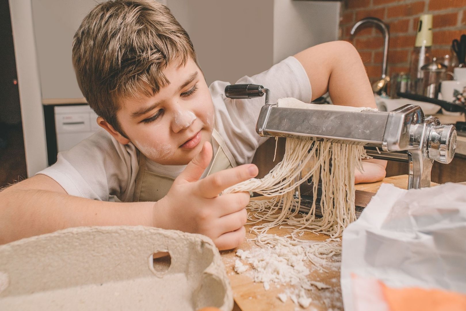 Jongen maakt verse pasta met een pastamachine op een bebloemd aanrecht