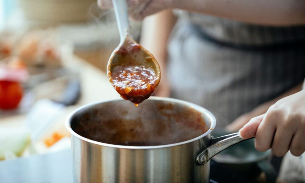 Lepel met warme rode saus boven een dampende steelpan